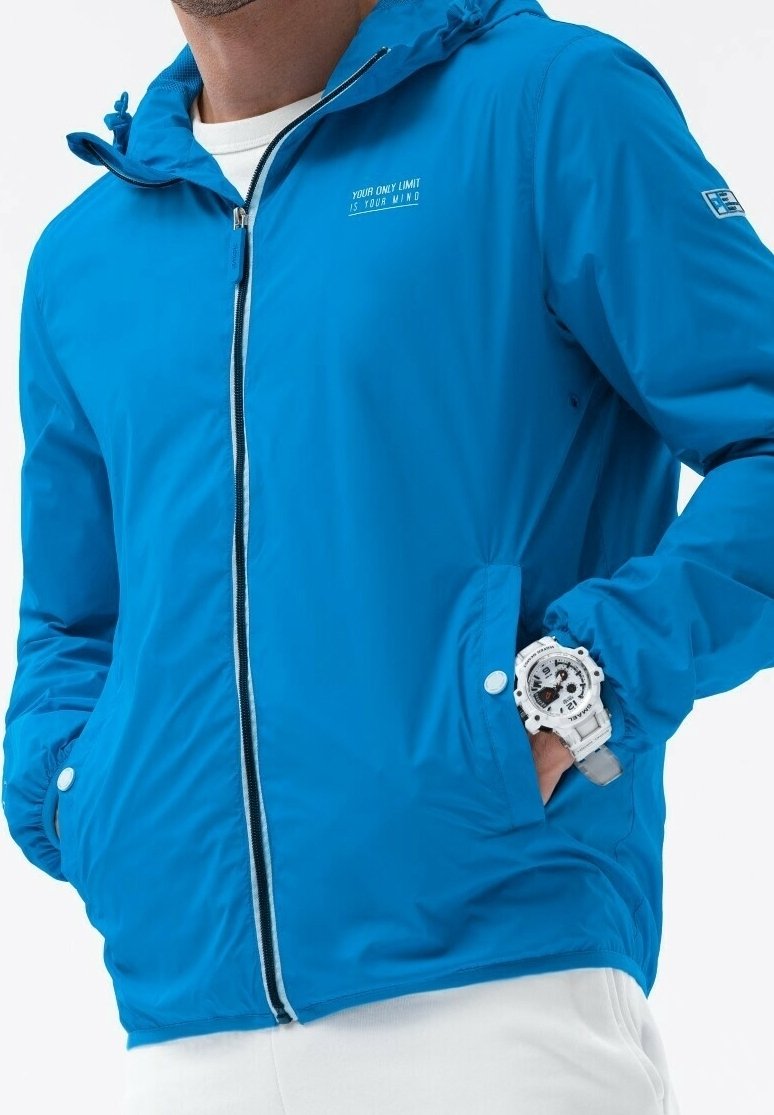 Blå letvægtsjakke med lynlåslukning foran, der har hætte, elastiske manchetter og et lille hvidt tekstmotiv på brystet.