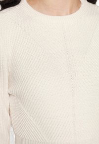 Pull en maille crème avec un motif texturé en côtes, col rond et coutures angulaires pour un design structuré.