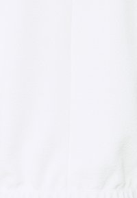 Bílá tkanina s hladkým, texturovaným povrchem. Obsahuje jemný diagonální vzor a na spodním okraji záhyby s elastickou vsadkou.