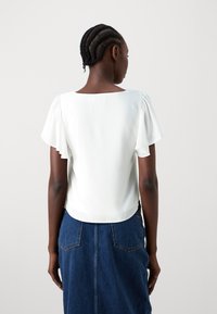 White short-sleeve blouse with gathered shoulders, smooth texture, and a square neckline, paired with a blue denim skirt.