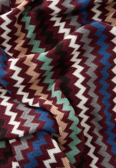 Tissu tricoté doux avec motif zigzag coloré dans des tons bordeaux, bleu, vert, beige, noir, blanc et gris, présenté en plis.
