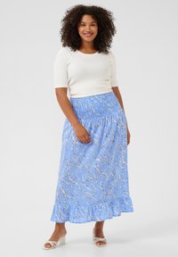 Lichtblauwe maxi rok met een golvende witte patroon, smocktail, en gerimpelde zoom. Gecombineerd met een aansluitend wit topje en lichtgekleurde sandalen.