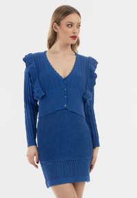 Abito blu lavorato a maglia con spalline arricciate, scollatura a V e dettagli con bottoni. Motivi testurizzati su tutto l'indumento. Design aderente.