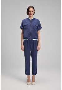 Marintvådelad outfit bestående av en kortärmad zip-up jacka med två framfickor och matchande tajta byxor, accentuerade med en randig fåll.