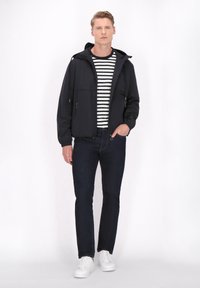 Zwarte hoodie met ritszakken, gecombineerd met een gestreept shirt. Donkere spijkerbroek en witte sneakers maken de look compleet. Eenvoudig ontwerp en kleuren.