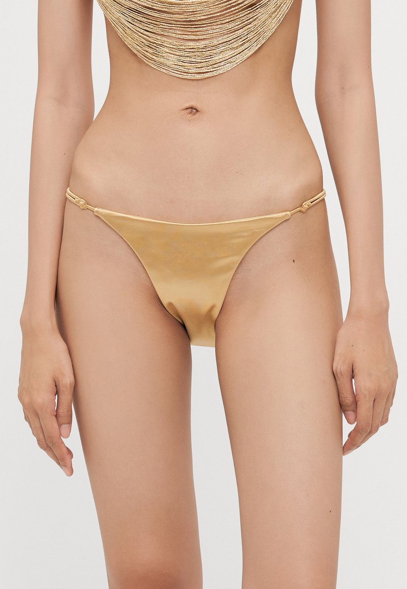 Auksinės satino bikini kelnaitės su lygiu paviršiumi, žemas juosmuo ir reguliuojamos slankiosios detalės. Pasižymi minimalios aprėpties stiliumi.