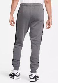 Pantaloni felpati grigi con pannelli laterali neri, vestibilità affusolata, vita elastica e polsini a coste, abbinati a scarpe da ginnastica nere e bianche.