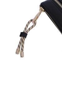 Accesorio de cuero negro con un zipper dorado. El tirador del zipper tiene un cordón trenzado en beige y negro con extremos metálicos, añadiendo textura y detalle.
