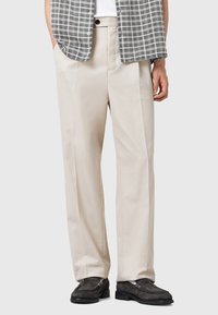 Beige tailored trousers with a smooth texture, featuring a relaxed fit and side pockets. Paired with a gray checkered shirt.