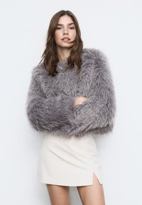 Blød, grå, oversized sweater med tykke ærmer, kombineret med en cremefarvet mininederdel med sideslids. Blød tekstur og luksuriøst udseende.