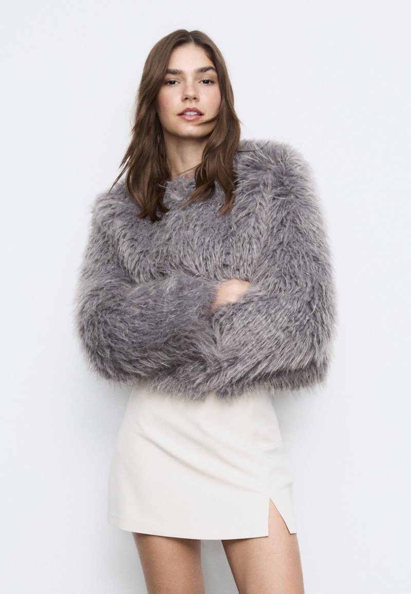 Blød, grå, oversized sweater med tykke ærmer, kombineret med en cremefarvet mininederdel med sideslids. Blød tekstur og luksuriøst udseende.