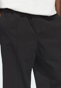 Μαύροι παντελόνες από ελαφρύ ύφασμα, με πλαϊνές τσέπες και λεία υφή. Η μέση έχει απλή, ελαστική τελειότητα.