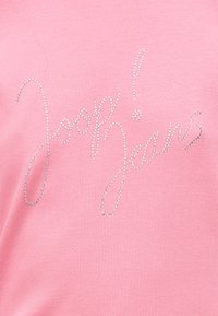 Ροζ ριμπ ύφασμα με τις λέξεις «Joupy!» και «Jeans» γραμμένες με καλλιγραφικά μικρές ασημένιες στρας.