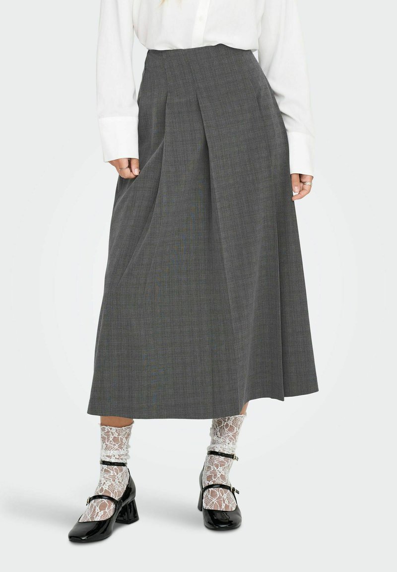 Falda plisada gris con un patrón texturizado, que presenta una cintura alta y una silueta fluida. Combinada con zapatos de tacón negros y calcetas. 