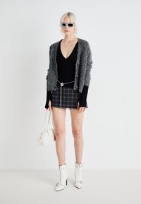 Grå strikket cardigan med gullknapper, svart v-hals topp, rutete mini skjørt, sølvkjede belte, hvit veske og ankel støvler med nagler.