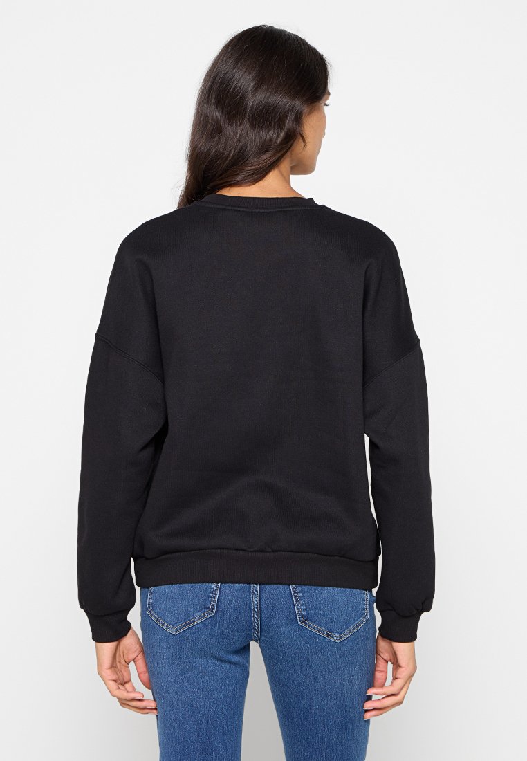 Sweatshirt noir à texture côtelée, coupe surdimensionnée et manches longues. Associé à un jean bleu clair, mettant en avant un style décontracté.