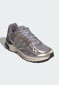 Sport shoe with a gray mesh upper and metallic gold accents, featuring a cushioned sole, lace-up design, and three striped logo detail.