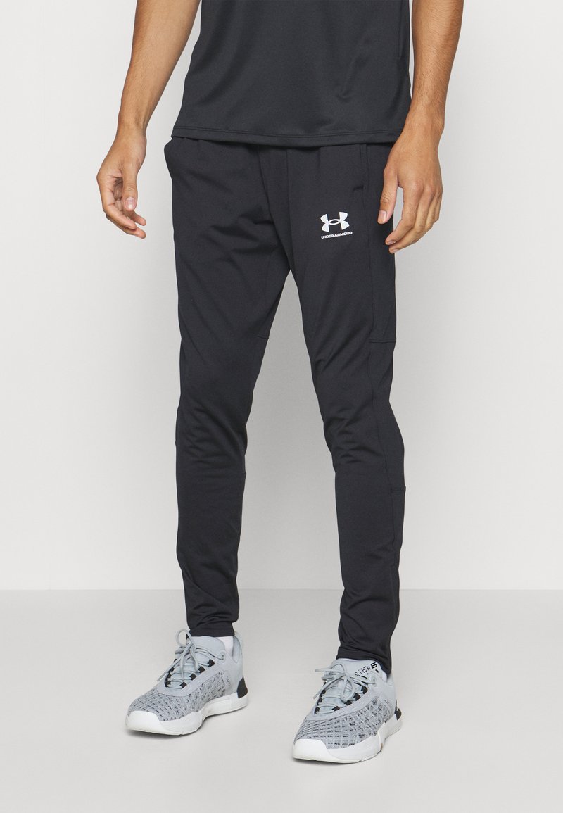 Czarne spodnie sportowe o slim fit, wykonane z gładkiego materiału. Posiadają białe logo na lewym udzie oraz boczne kieszenie. Zestawione z szarymi butami sportowymi.