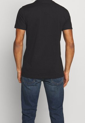 Black short-sleeve t-shirt made from cotton, featuring a round neckline and a relaxed fit, paired with dark blue denim jeans.
