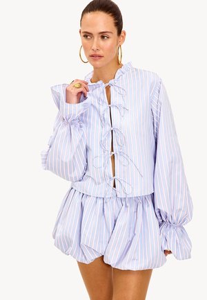 Blouse rayée bleu clair avec manches bouffantes, col à volants et liens à l'avant. Tissu doux avec une coupe ample et fluide.