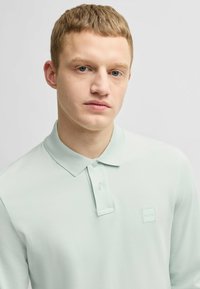 Vaaleanvihreä polo-paita, joka on valmistettu teksturoidusta kankaasta. Paidan rinnassa on kaksi nappia ja pieni kohokuvioitu logo vasemmalla puolella.