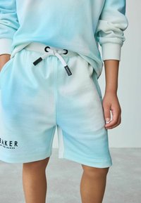 Pantalones cortos de sudadera de gradiente azul claro con cinturilla elástica, cordón y logo "BAKER" en la pierna izquierda. Tejido suave, similar al algodón.