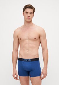 Plave pamučne bokserice s crnim elastičnim pojasom koji sadrži plavi Levi's logo. Glatka tekstura, prilagodljiv oblik.