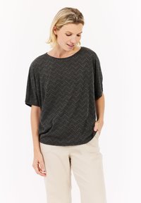 Šedý textured krátký rukáv top s chevronovým vzorem, kulatým výstřihem a uvolněným střihem, v kombinaci se světlými béžovými kalhotami.