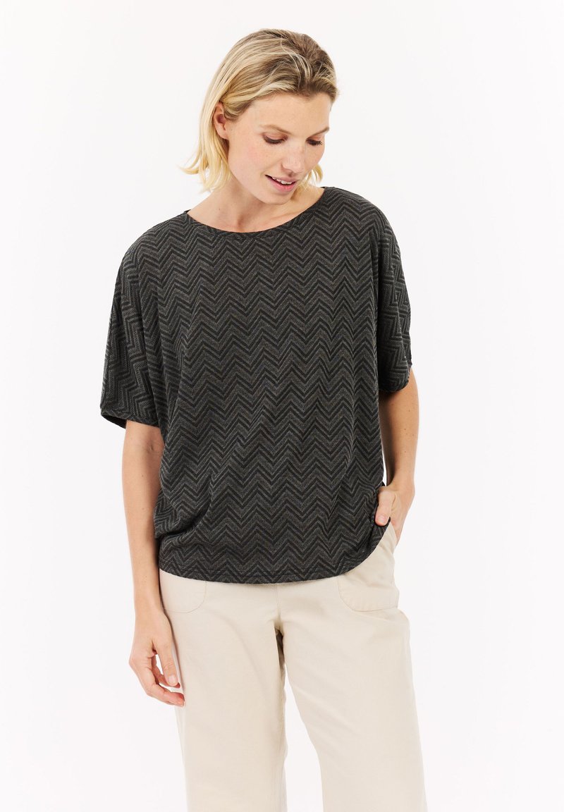 Šedý textured krátký rukáv top s chevronovým vzorem, kulatým výstřihem a uvolněným střihem, v kombinaci se světlými béžovými kalhotami.