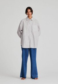 Striped button-up shirt with a collar and front pocket, in light colors. Paired with wide-leg blue jeans. Soft cotton texture.