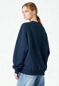 Sweat-shirt bleu marine à coupe décontractée, avec poignets et ourlet côtelés, et encolure arrondie. Texture douce sans motifs ni graphiques visibles.