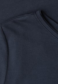 Gros plan d'un tissu bleu foncé montrant la couture d'épaule et l'encolure ronde d'un vêtement à manches longues.