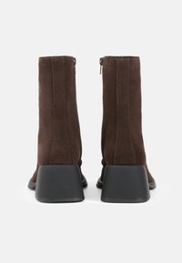 Brown suede ankle boots with a square-shaped black heel and side zipper, featuring vertical stitching details along the back.