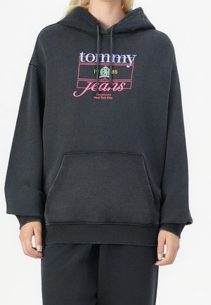 Sweat à capuche oversize gris foncé avec poche avant, logo multicolore "tommy jeans" et texte "Established New York City" porté par une personne.