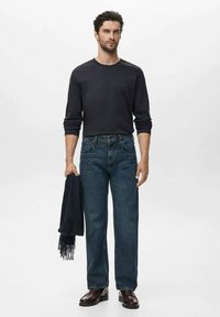 Dunkelbluse mit langen Ärmeln, blaue Jeans und bordeauxfarbene Schuhe. Hält einen dunklen Schal. Einfaches Design, klassischer Schnitt, strukturierter Stoff und standardmäßiger Schnitt.