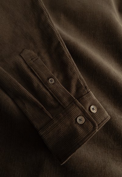 Brown corduroy fabric featuring vertical stripes, a placket with two buttons, and a textured finish. The fabric has a soft, fine ribbed pattern.