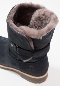 Botte d'hiver bleu foncé avec doublure en fourrure beige douce et épaisse, sangle réglable avec boucle métallique et semelle robuste brun clair.