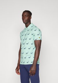 Light mint green polo shirt featuring a repeated dark navy golf club design. Short sleeves with a small yellow logo on the left arm.