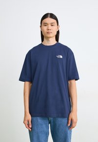Navy blå bomull T-skjorte med korte ermer og rund hals, med en liten hvit logo på venstre brystområde. Kombinert med blå jeans.