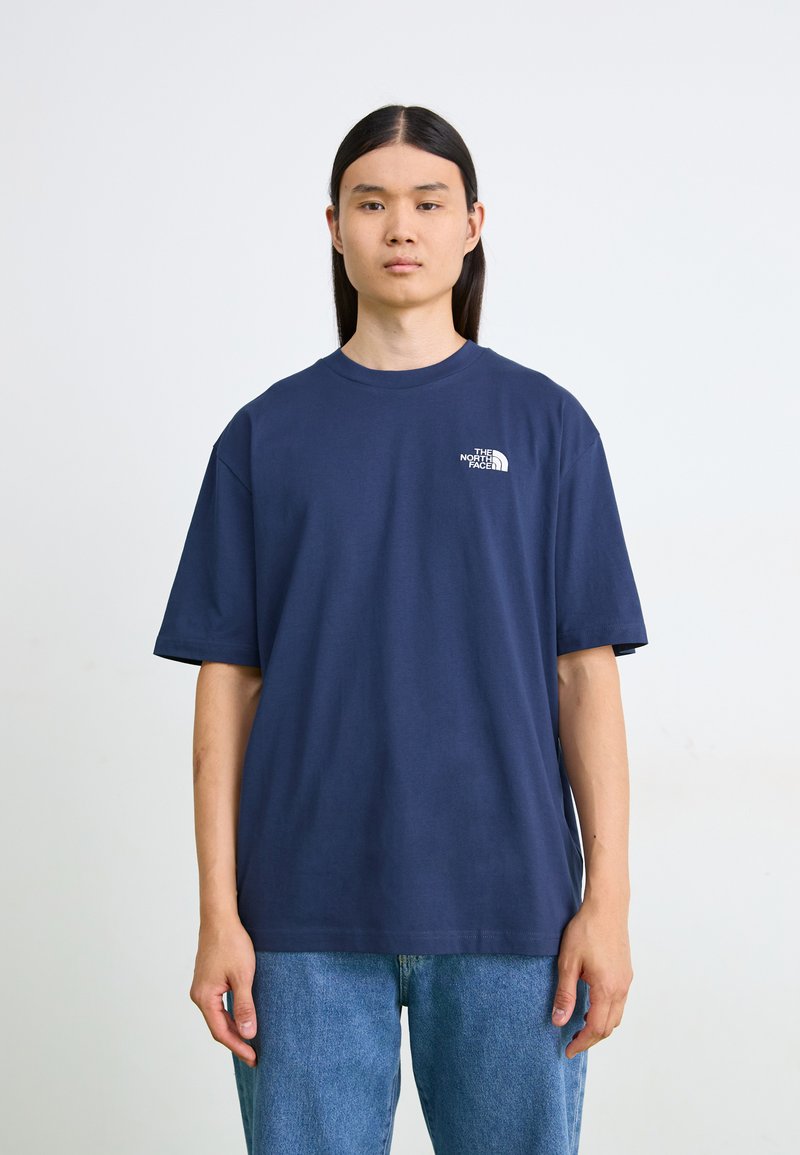 Navy blå bomull T-skjorte med korte ermer og rund hals, med en liten hvit logo på venstre brystområde. Kombinert med blå jeans.