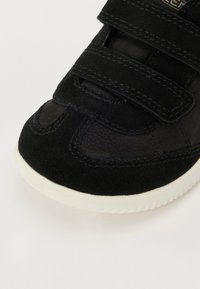 Sneaker nera con una combinazione di pelle scamosciata e pelle liscia, doppie cinghie in Velcro e suola in gomma bianca. Design della punta arrotondata.