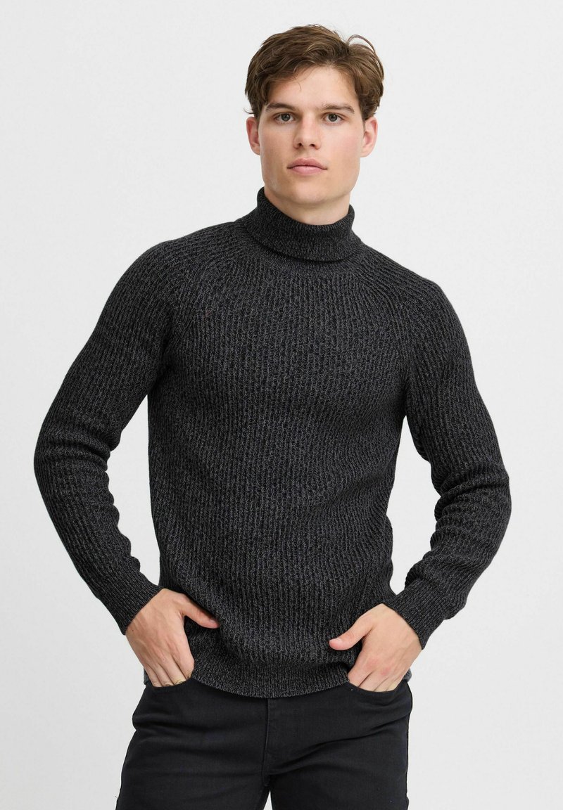 Schwarzer Rollkragenpullover aus strukturiertem Strick mit taillierter Passform und gerippten Bündchen, getragen von einem Model vor einem schlichten Hintergrund.