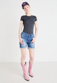 Siv bodi z kratkimi rokavi, modri jeans hlače s zavihanimi robovi, roza usnjeni čevlji v cowboy slogu s embosirano obdelavo in temna kapa.