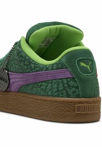 Sneaker verde in suede con parte superiore testurizzata, accenti viola e suola in gomma. Presenta un colletto imbottito e un'etichetta metallica attaccata.