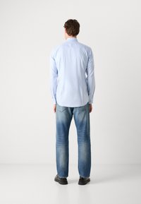 Camisa de manga larga a rayas en azul claro, con puños abotonados, corte relajado, combinada con vaqueros azules desgastados y zapatos negros. Vista trasera.