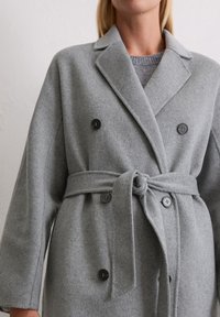 Grau melierter Wollmix-Mantel mit doppelter Knopfleiste, Reverskragen, seitlichen Taschen und einem gebundenen Gürtel in der Taille, mit schwarzen Knöpfen.