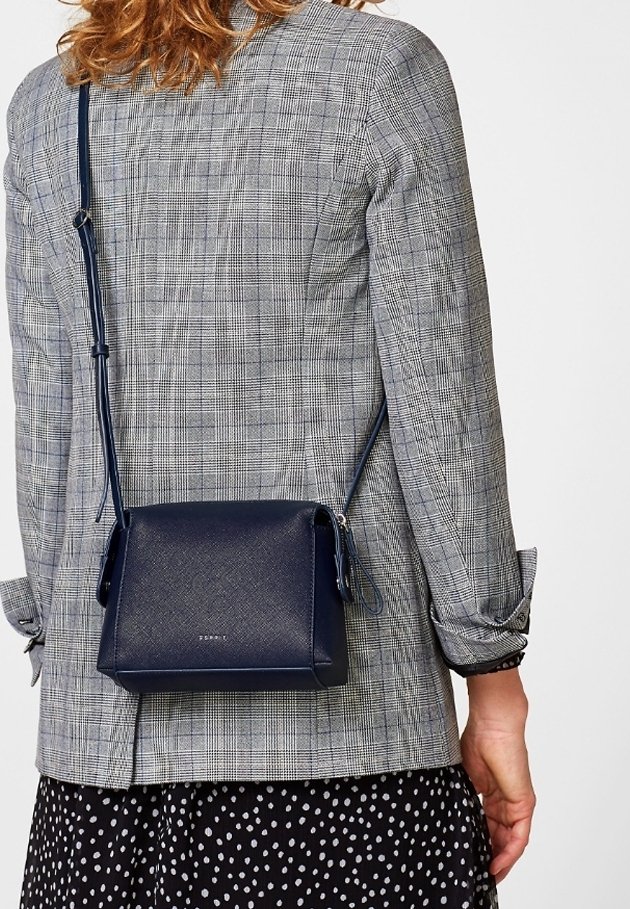 Borsa a tracolla blu navy con una forma strutturata, materiale sintetico testurizzato e tracolla regolabile, posizionata contro un giaccone grigio a quadri.