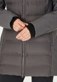Grå pufferjakke med kviltet design. Funktioner en frontlynlås, sorte manschette accenter og tykk stoftekstur for varme.
