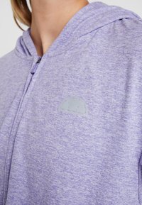 Felpa con cappuccio di un morbido colore viola chiaro, realizzata in tessuto testurizzato, dotata di chiusura con zip e un logo discreto a contrasto sul petto.
