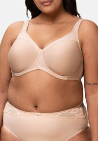 Béžová podprsenka s kosticemi, hladkými košíčky, širokými ramínky a sportovním designem. V páru s odpovídajícími vysokými kalhotkami zdobenými krajkou.